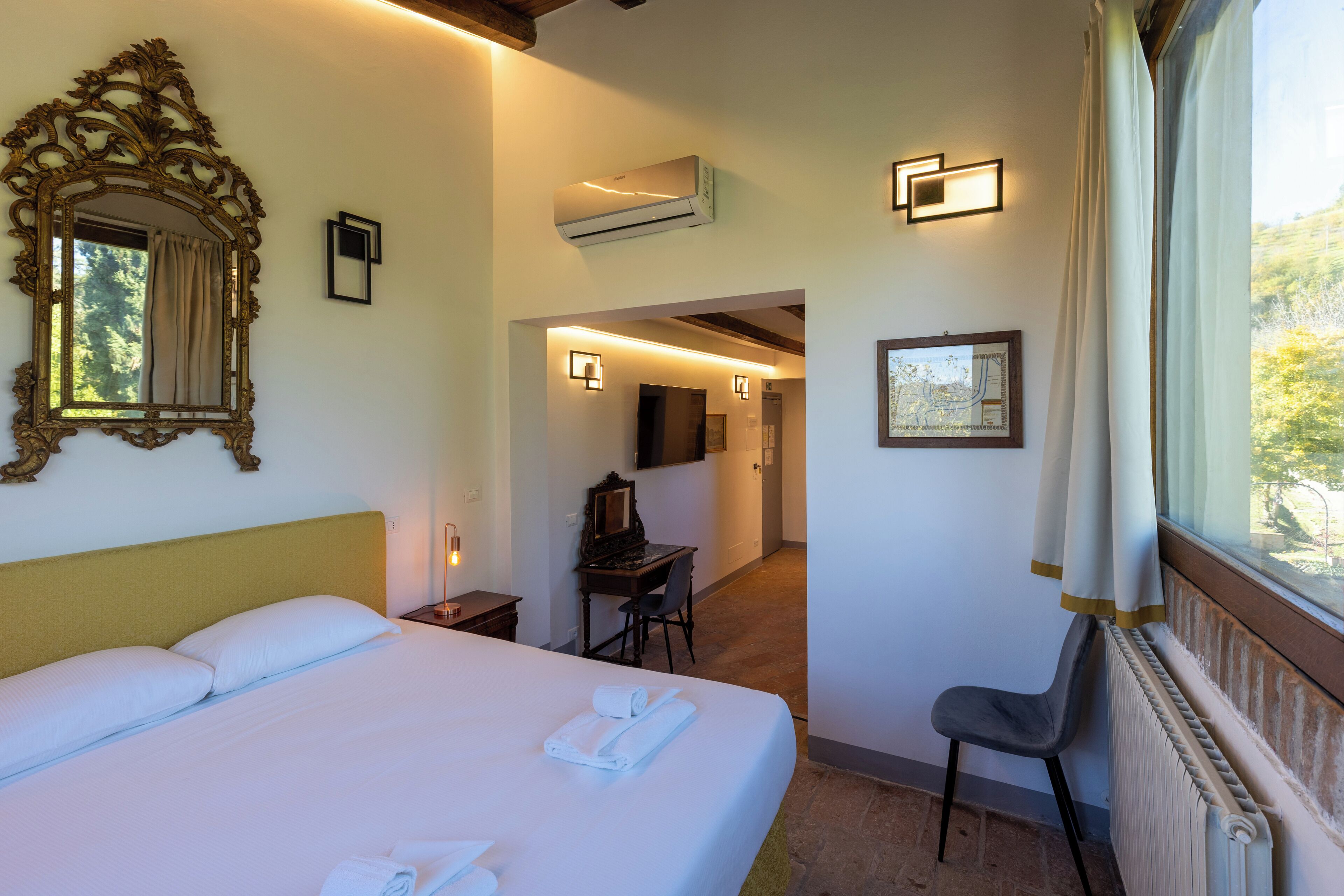 A hotel room with a large bed, a desk, a chair, a mirror, and a window with curtains.