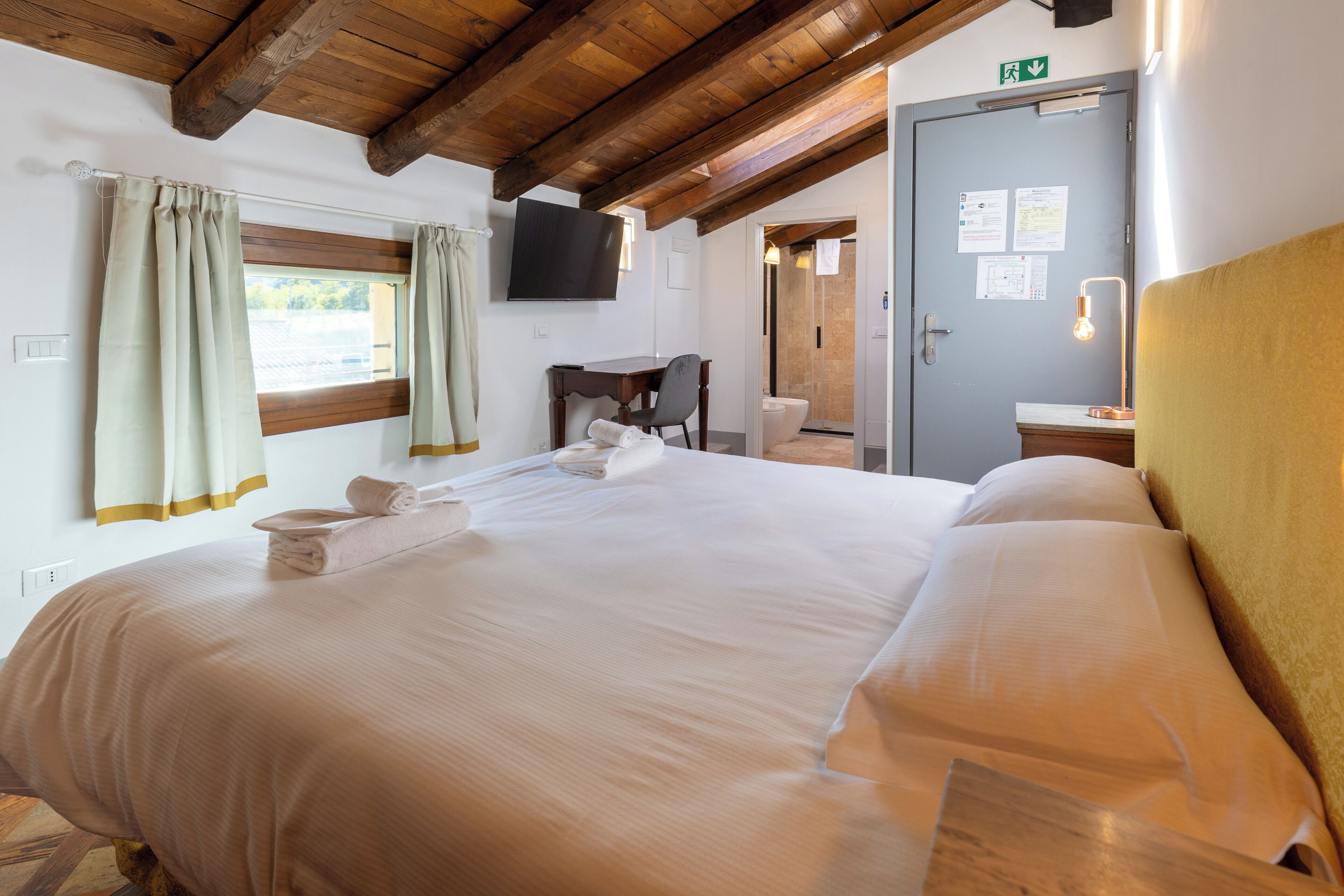 A hotel room with a large bed, a desk, a television, and a bathroom visible through an open door.