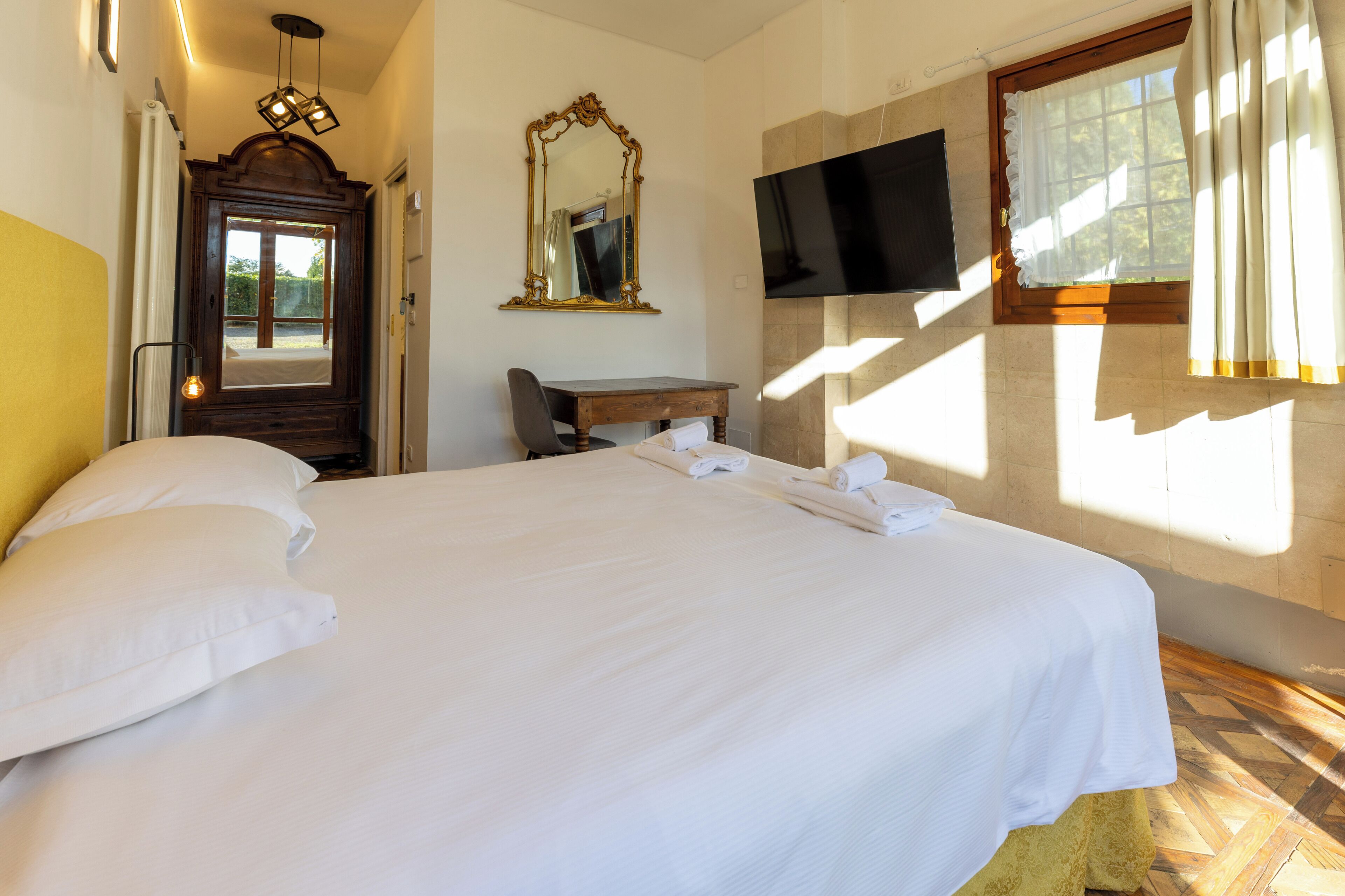 Una habitación de hotel con una cama grande, un escritorio, un espejo, un televisor y una ventana con cortinas.