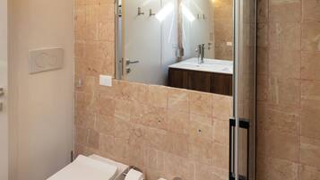 Une salle de bain comprenant des toilettes, un bidet, un lavabo et une douche à parois de verre.