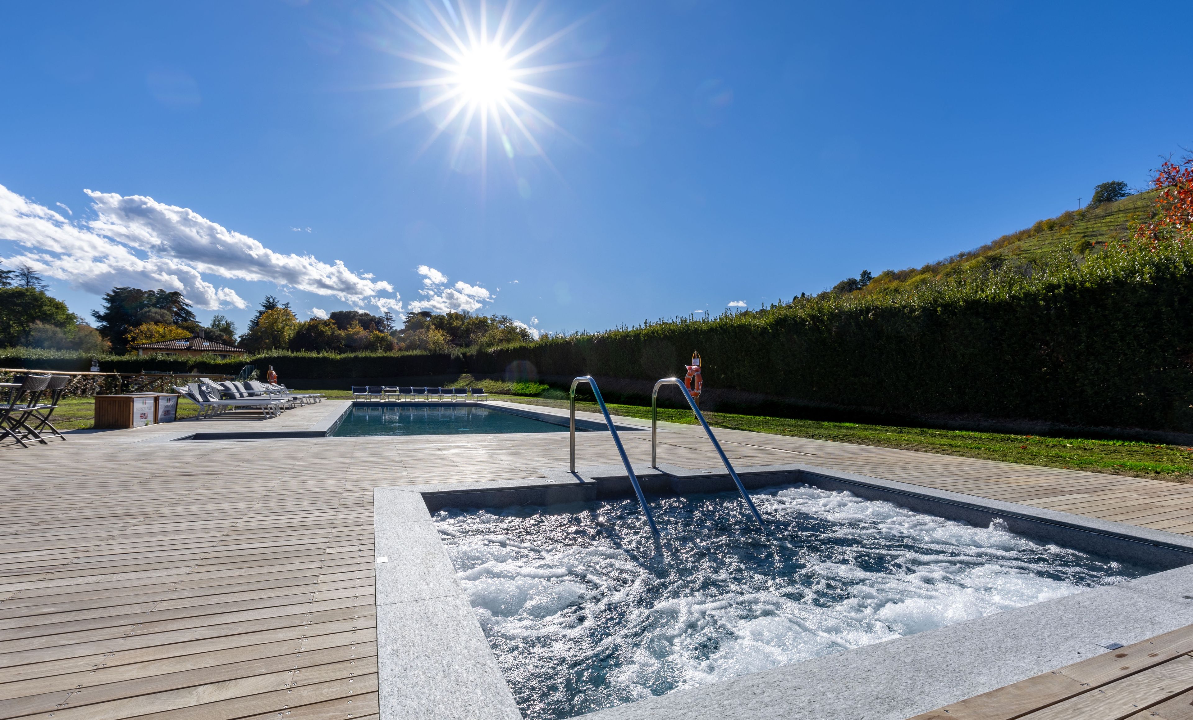 Area piscina con vasca idromassaggio, lettini e un solarium in legno.