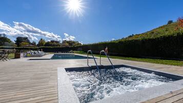 Area piscina con vasca idromassaggio, lettini e un solarium in legno.