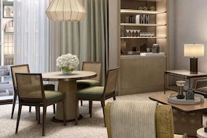 A hotel room with a round dining table, four chairs, a vase of flowers, a lamp, a bookshelf, and a view of the city. - Giza Palace Hotel & Spa - The Leading Hotels Of The World (Sheikh Zayed City)
