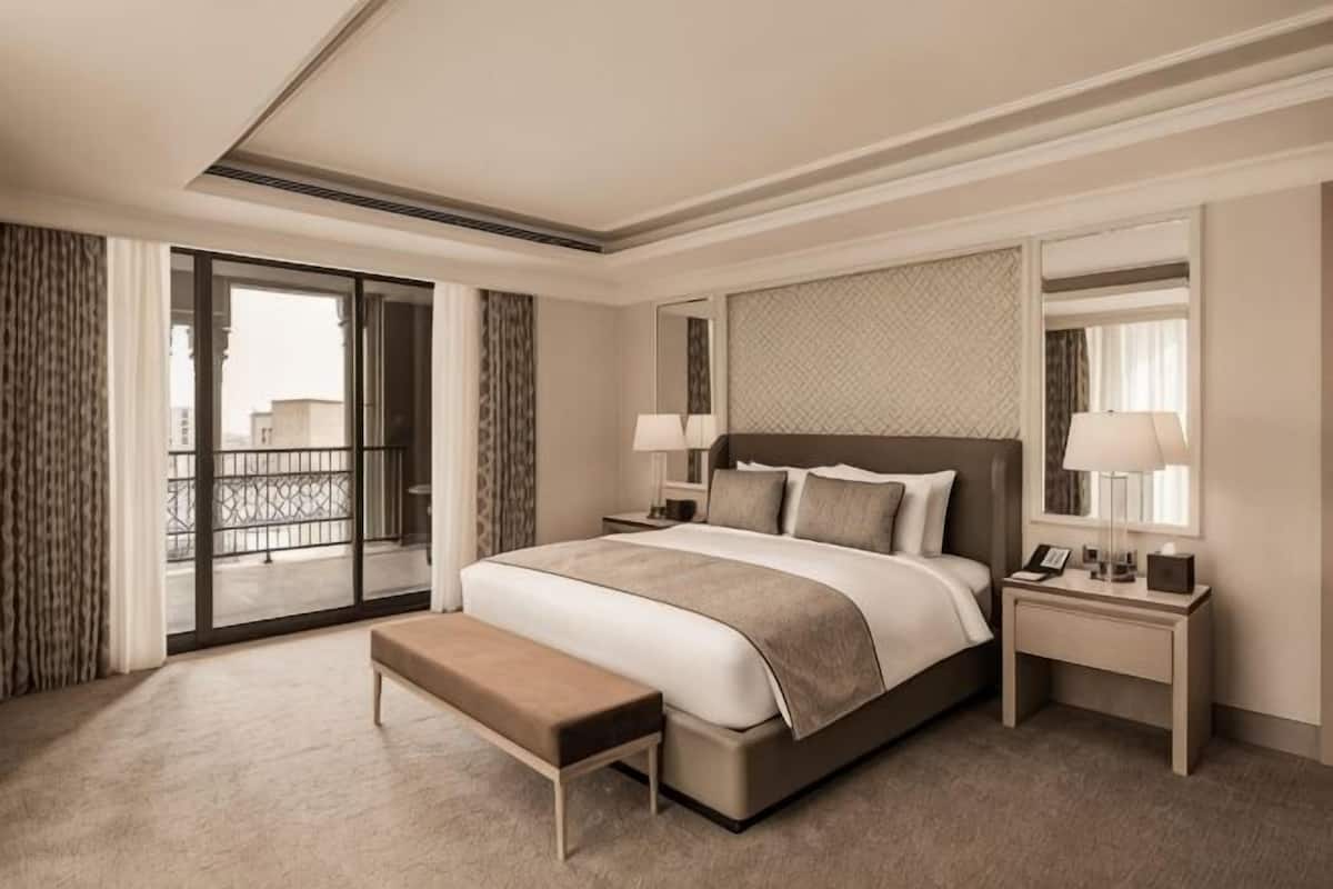 Ein Hotelzimmer mit einem großen Bett, einer Sitzbank, einem Nachttisch, einem Spiegel und Blick durch eine Balkontür.
