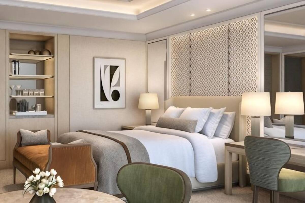 Ein modernes Hotelzimmer mit einem großen Bett, Nachttischen, einem Schreibtisch und einem Sessel. Ein Bücherregal und eine dekorative Wandverkleidung sind ebenfalls vorhanden.