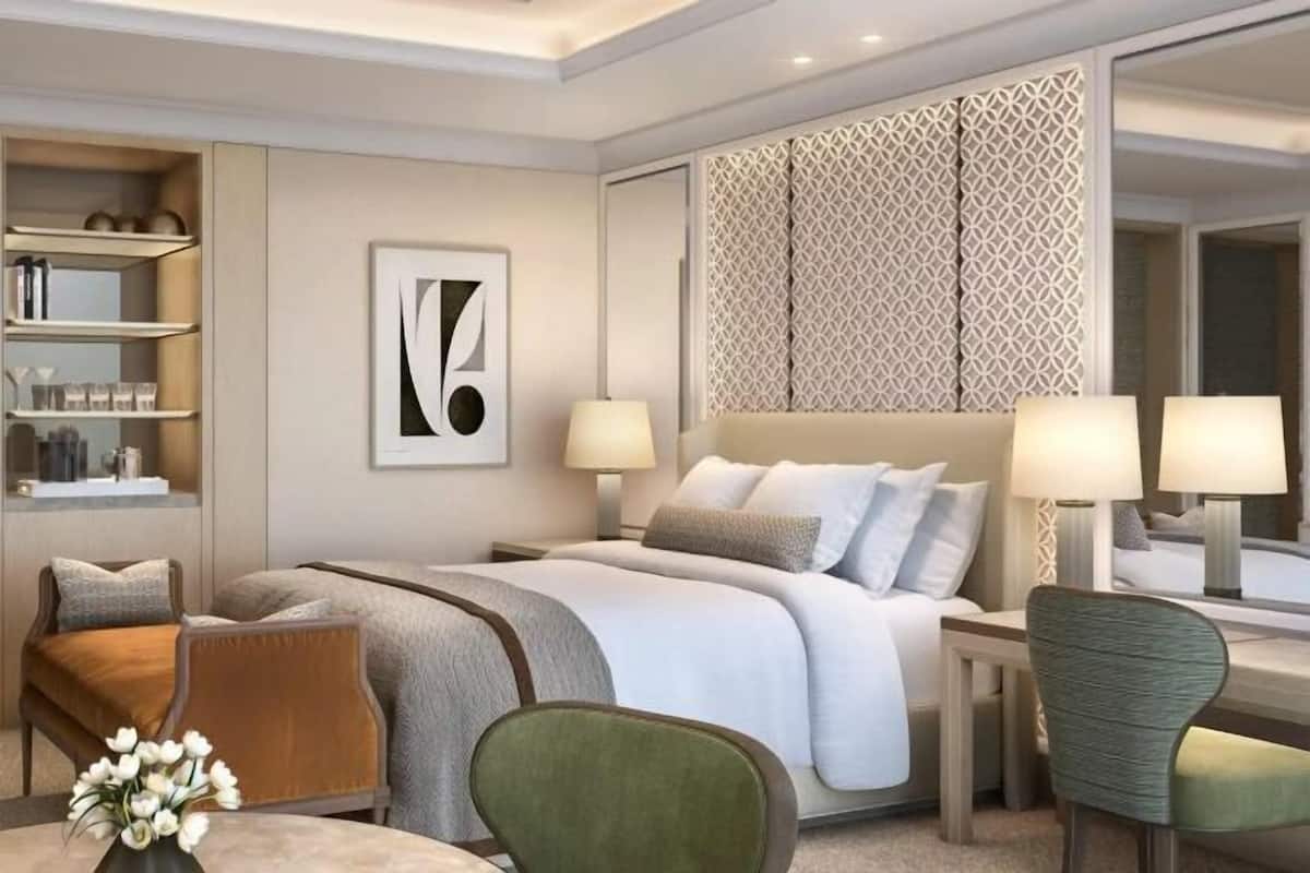 Ein modernes Hotelzimmer mit einem großen Bett, zwei Nachttischen inklusive Lampen, einem grünen Sessel, einem kleinen runden Tisch mit Blumen und einer dekorativen Wandverkleidung.