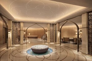 A modern hotel lobby with a central seating area, a reception desk, and a decorative water feature.