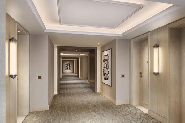 A hotel corridor with a patterned carpet, framed artwork on the walls, and light fixtures on the ceiling.