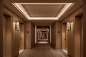 A long, narrow hallway with wooden doors on both sides, recessed lighting, and a patterned carpet.