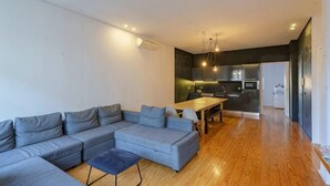 A modern living room with a sectional sofa, a dining table, and a kitchen area in the background. - N Apartments - Luís (Porto)