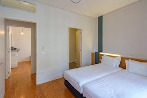 A hotel room with a double bed, a wooden floor, and a door leading to a bathroom.