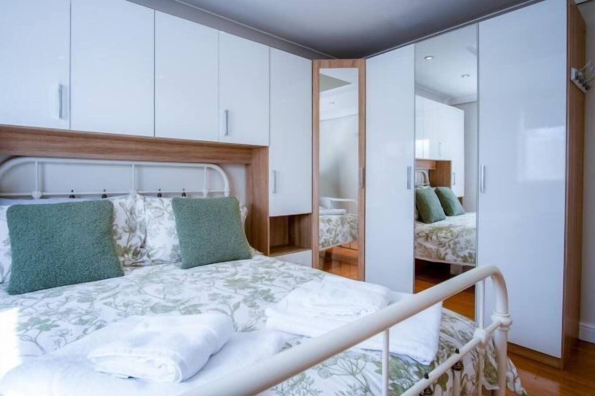 A modern bedroom with a bed, a wooden headboard, and a wardrobe with a mirror.