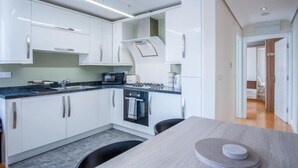 Una cucina moderna con mobili bianchi, un piano di lavoro nero e un fornello. C'è un tavolo da pranzo con piatti e una sedia.