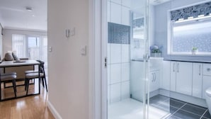 Un bagno moderno con box doccia in vetro, mobili bianchi e una finestra decorata con motivi floreali.