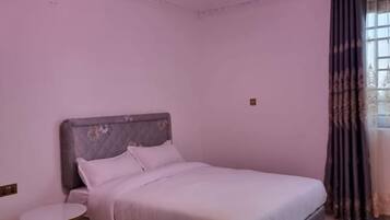 Une chambre à coucher avec un lit, une table ronde et une fenêtre avec des rideaux.