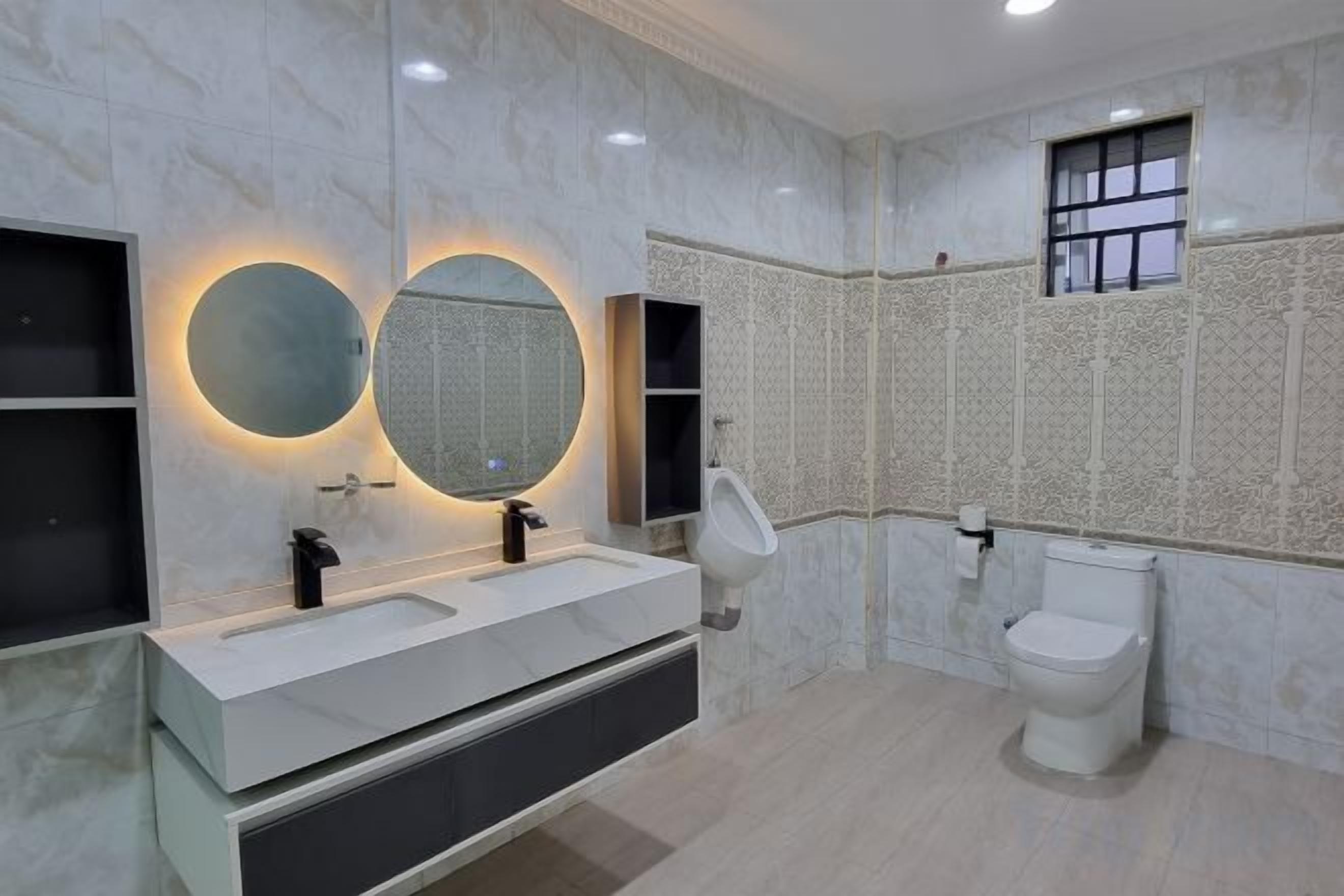 Une salle de bain avec un meuble-lavabo blanc, deux miroirs ronds, des toilettes et une fenêtre.