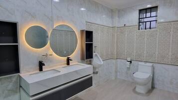 Une salle de bain avec un meuble-lavabo blanc, deux miroirs ronds, des toilettes et une fenêtre.