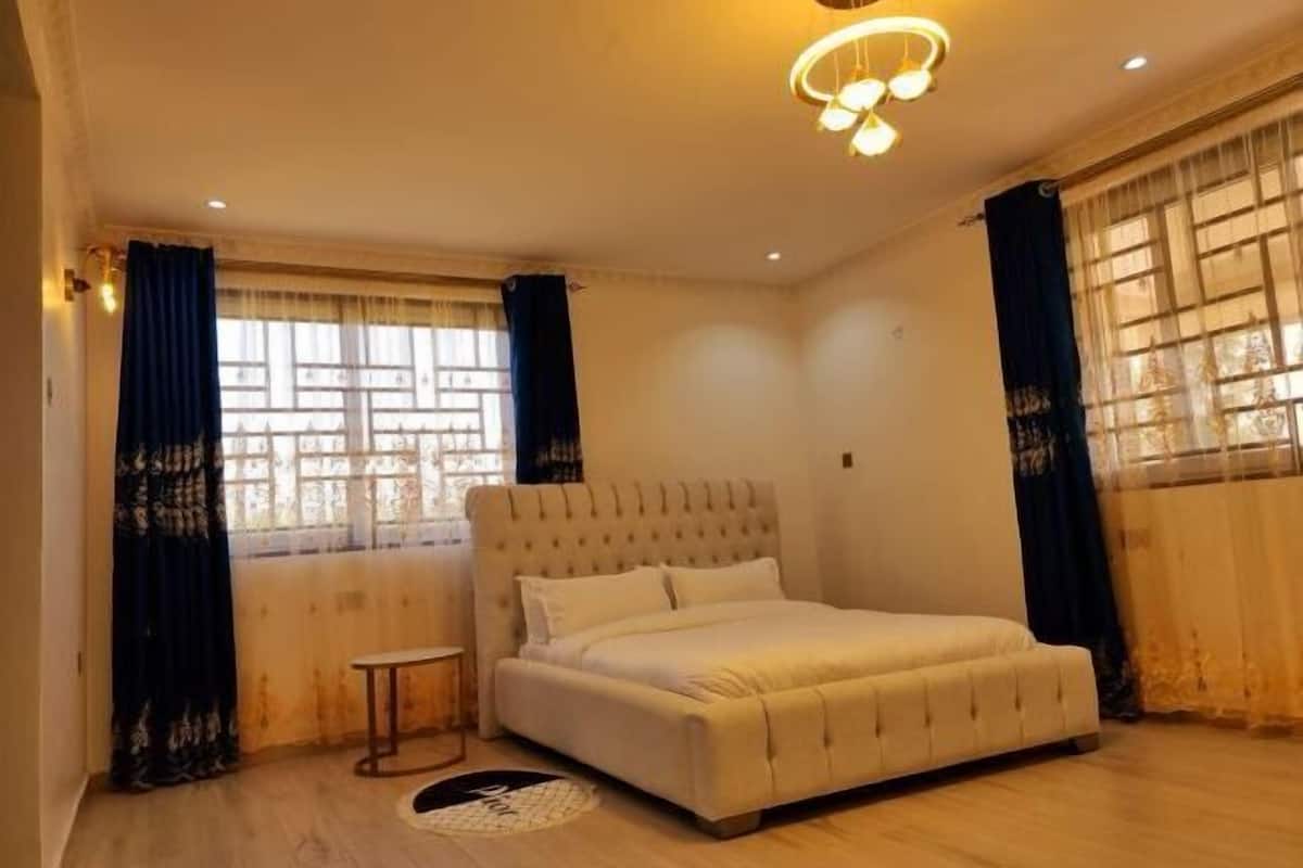 A bedroom with a large bed, a small bedside table, and a window with curtains.