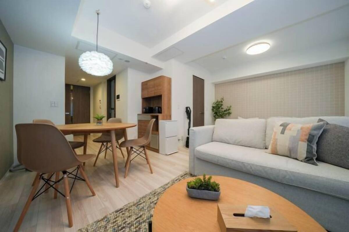 A modern living room with a sofa, coffee table, dining table, chairs, and a kitchen area.