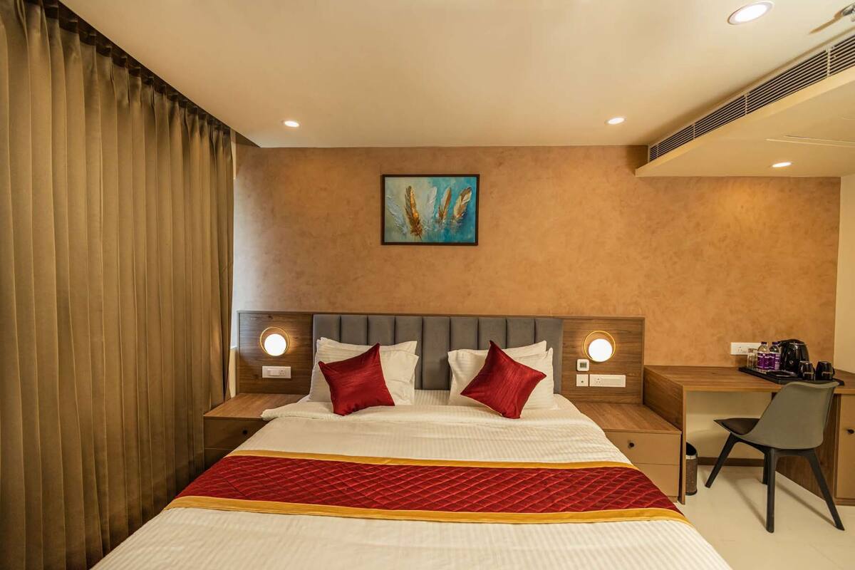 Een hotelkamer met een groot bed, twee nachtkastjes met lampen, een bureau met stoel, en een schilderij aan de muur.