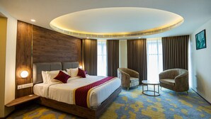A hotel room with a large bed, two armchairs, a small table, and a modern ceiling light fixture. - Ascot Hotel Calicut (Kozhikode)