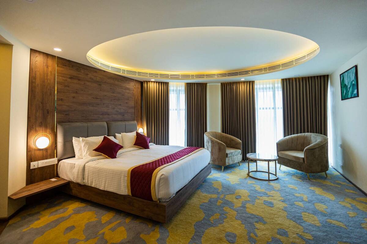 Een hotelkamer met een groot bed, twee fauteuils, een kleine tafel en een moderne plafondlamp.
