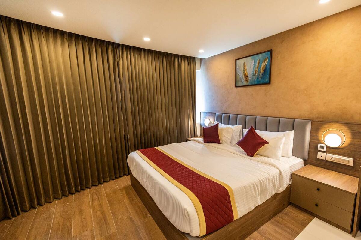 Een hotelkamer met een groot bed, houten vloeren, een hoofdbord met ingebouwde verlichting, een nachtkastje met lade en een schilderij aan de muur.