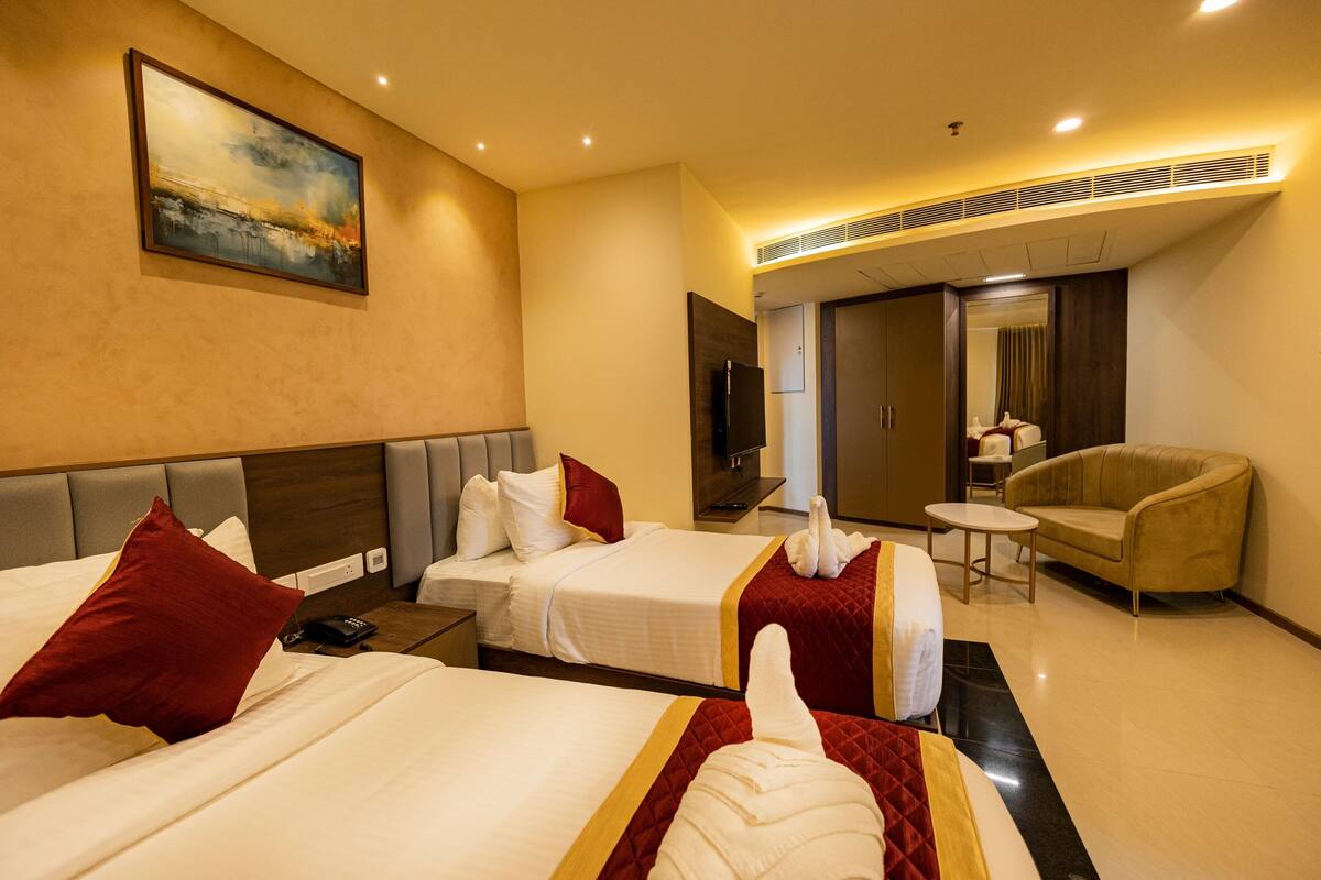Een hotelkamer met twee bedden, een televisie, een bank en een schilderij aan de muur.