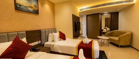 A hotel room with two beds, a TV, a sofa, and a painting on the wall.