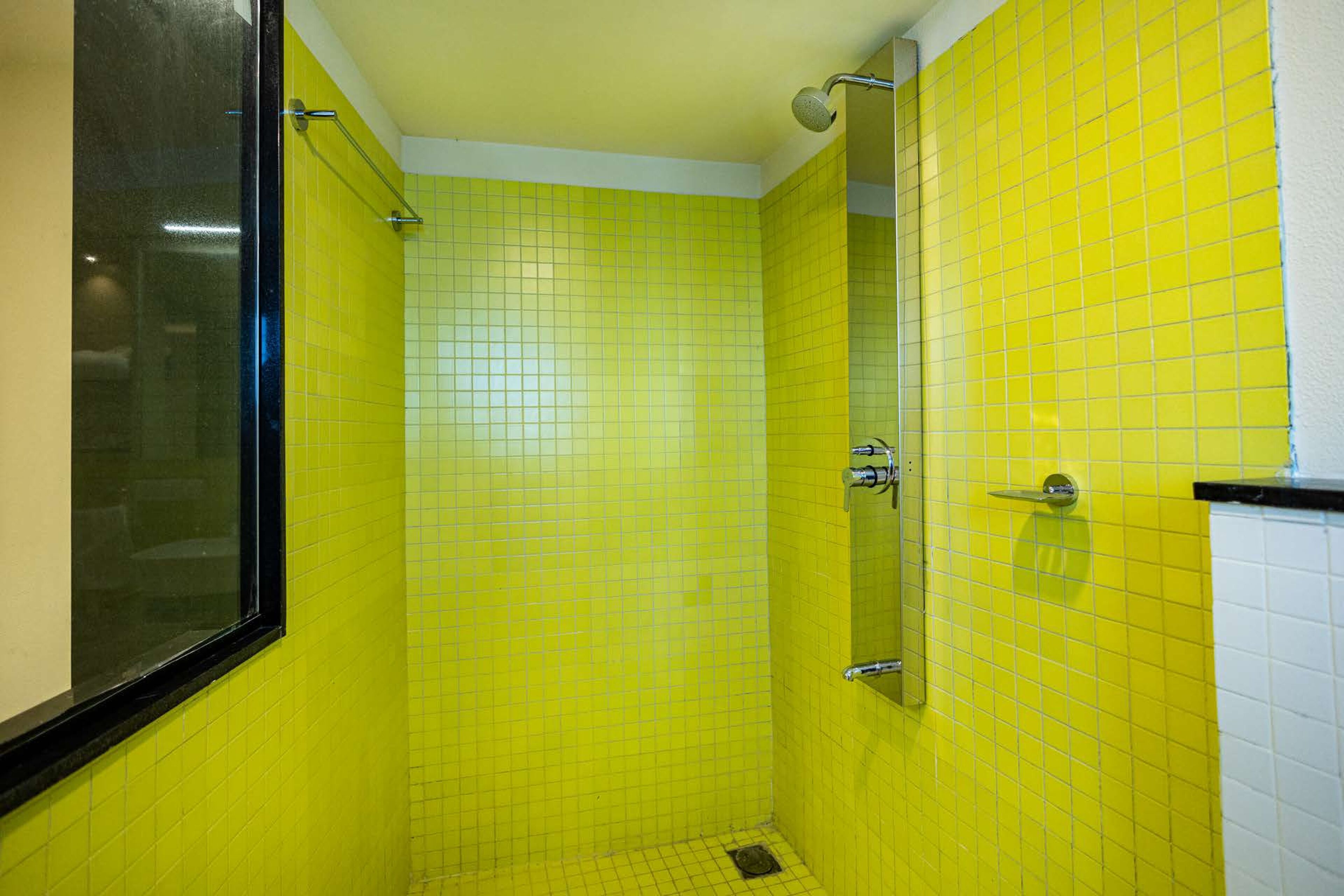 Un baño con paredes de azulejos amarillos y una ventana con marco negro.