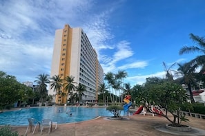 Ett hotell med en swimmingpool, palmer och en hög byggnad i bakgrunden.