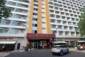 Ein mehrstöckiges Hotel mit einer markanten roten und gelben Fassade, einem sichtbaren Eingang und einem parkenden Auto davor.