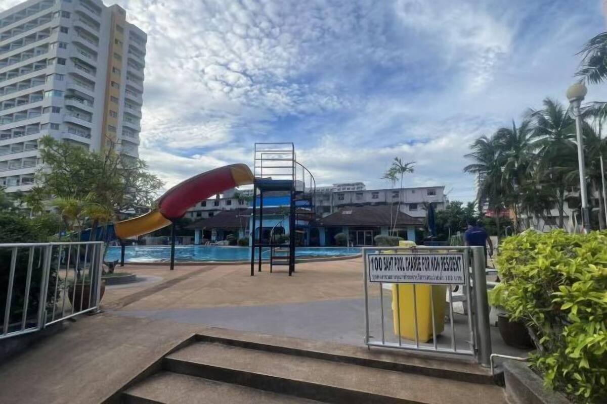 Un espace piscine avec un toboggan, entouré de bâtiments et de palmiers.