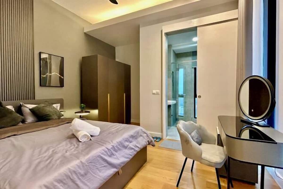 A modern hotel room with a bed, a desk, a chair, a mirror, and a wardrobe.