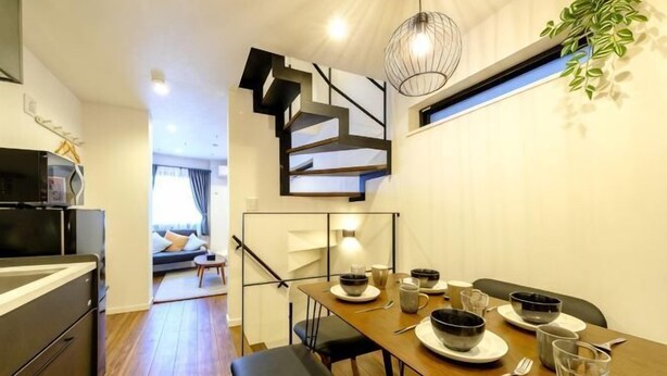 Une cuisine moderne avec une table à manger pour quatre personnes, un escalier et un coin salon à l’arrière-plan.