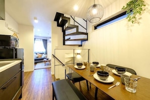 A modern kitchen with a dining table set for four, a staircase, and a living area in the background.
