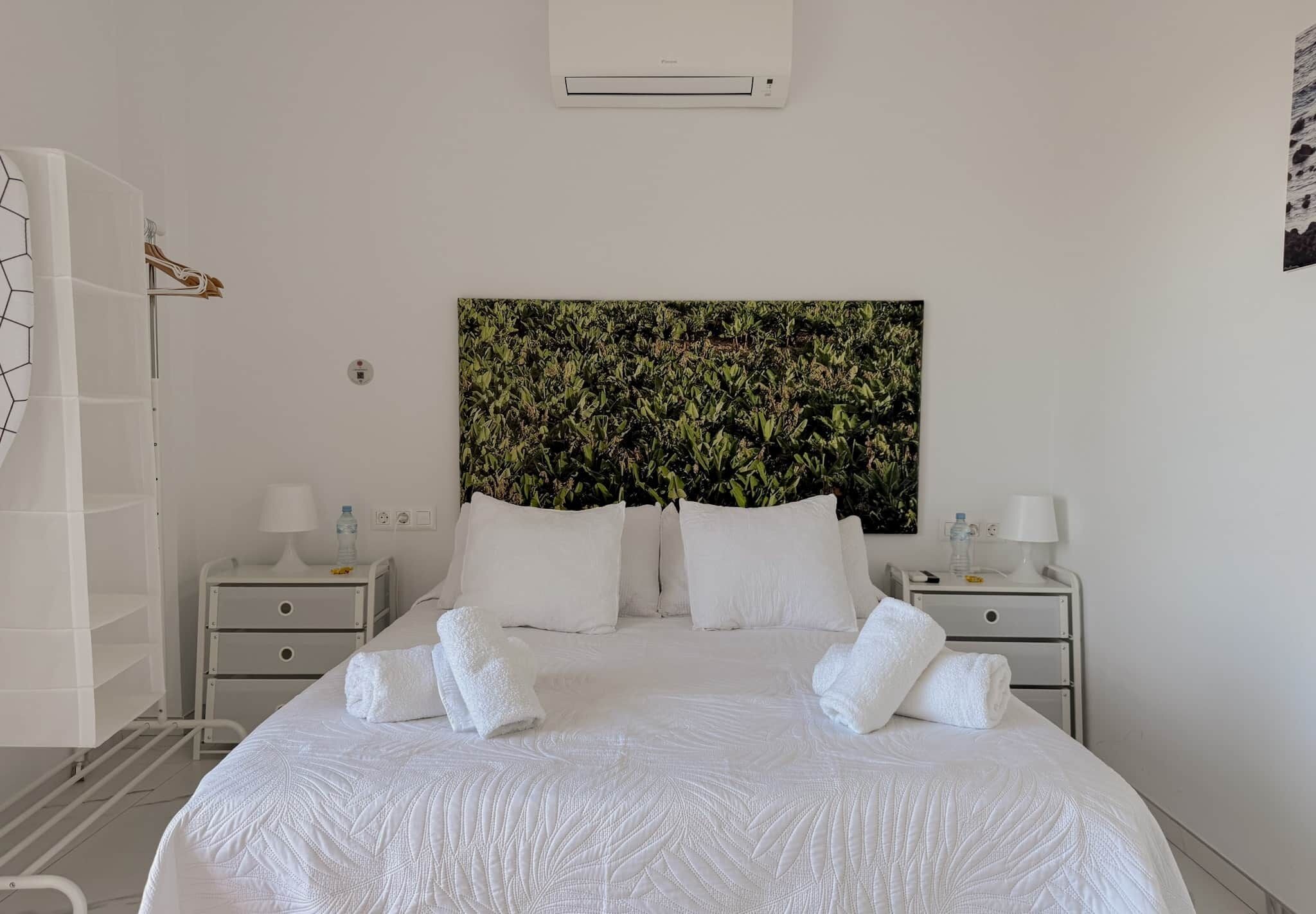 Camera d'albergo con un letto grande, due comodini con lampade, un condizionatore d'aria a parete e un grande quadro astratto sopra il letto.