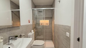 A modern bathroom with a glass-enclosed shower, a white sink, and a toilet.