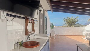 A kitchen with white tiles, a sink, and a wooden shelf with dishes.