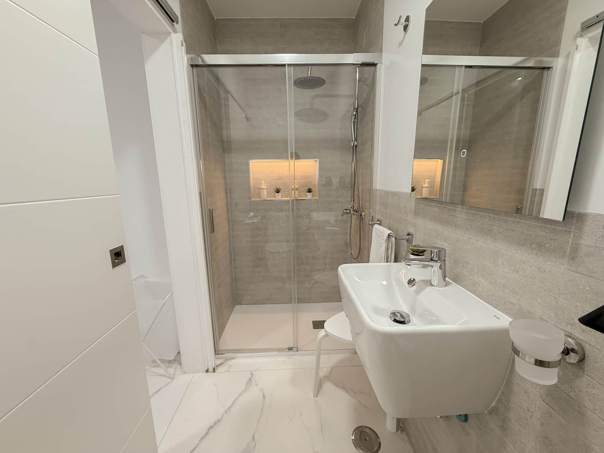 A modern bathroom with a glass-enclosed shower, a white sink, and a large mirror.