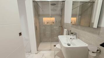 A modern bathroom with a glass-enclosed shower, a white sink, and a large mirror.