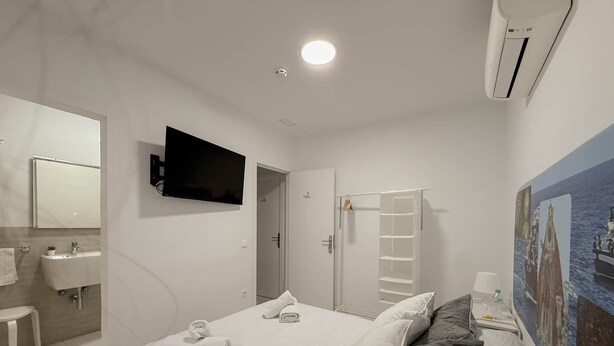 A hotel room with a bed, a TV mounted on the wall, a bathroom with a sink and mirror, and a painting on the wall.