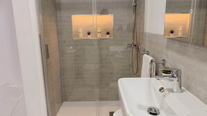 A modern bathroom with a glass-enclosed shower, a white sink, and a mirror above the sink.