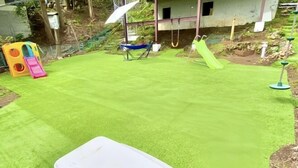 A green artificial turf area with a white table, a children's play structure, and a swing set. - Atami Tenku Villa Sky terrace (Atami)