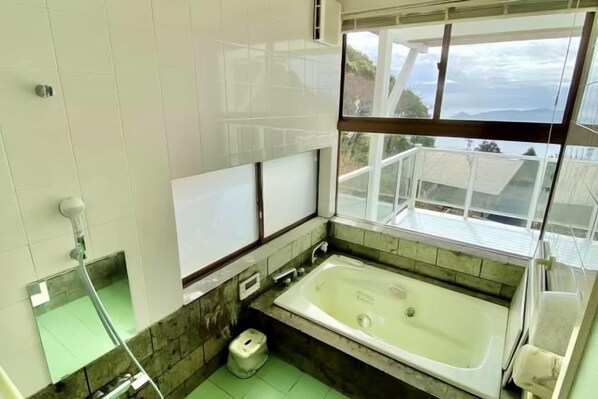A bathroom with a bathtub, a toilet, and a window with a view. - Atami Tenku Villa Sky terrace (Atami)