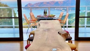A dining area with a long wooden table, chairs, and a view of the sea and mountains. - Atami Tenku Villa Sky terrace (Atami)