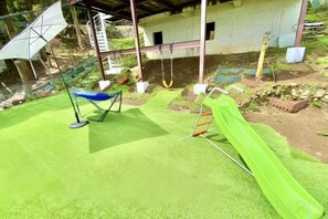 A green artificial turf area with a blue swing set and a green slide. - Atami Tenku Villa Sky terrace (Atami)
