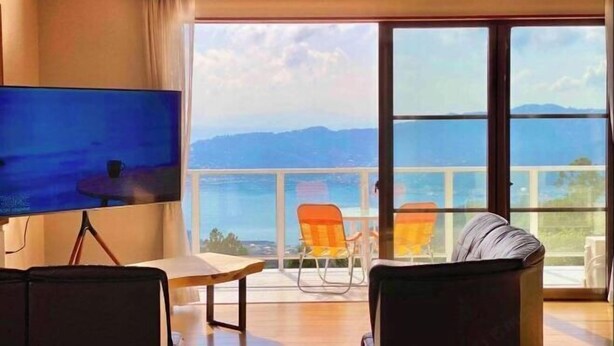 Een kamer met een grote televisie, twee stoelen, een tafel en een balkon met uitzicht op bergen.