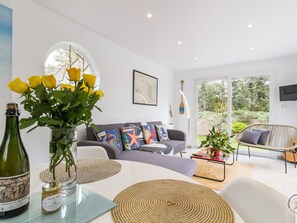 A modern living room with a sofa, a dining table, and a wicker chair. There is a bottle of wine on the table and a vase with yellow flowers. - Charming house with garden near the beach (Saint-Jean-de-la-Rivière)