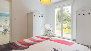 Un dormitorio con cama, lámpara colgante, puerta corrediza al exterior y una pequeña mesa con silla.
